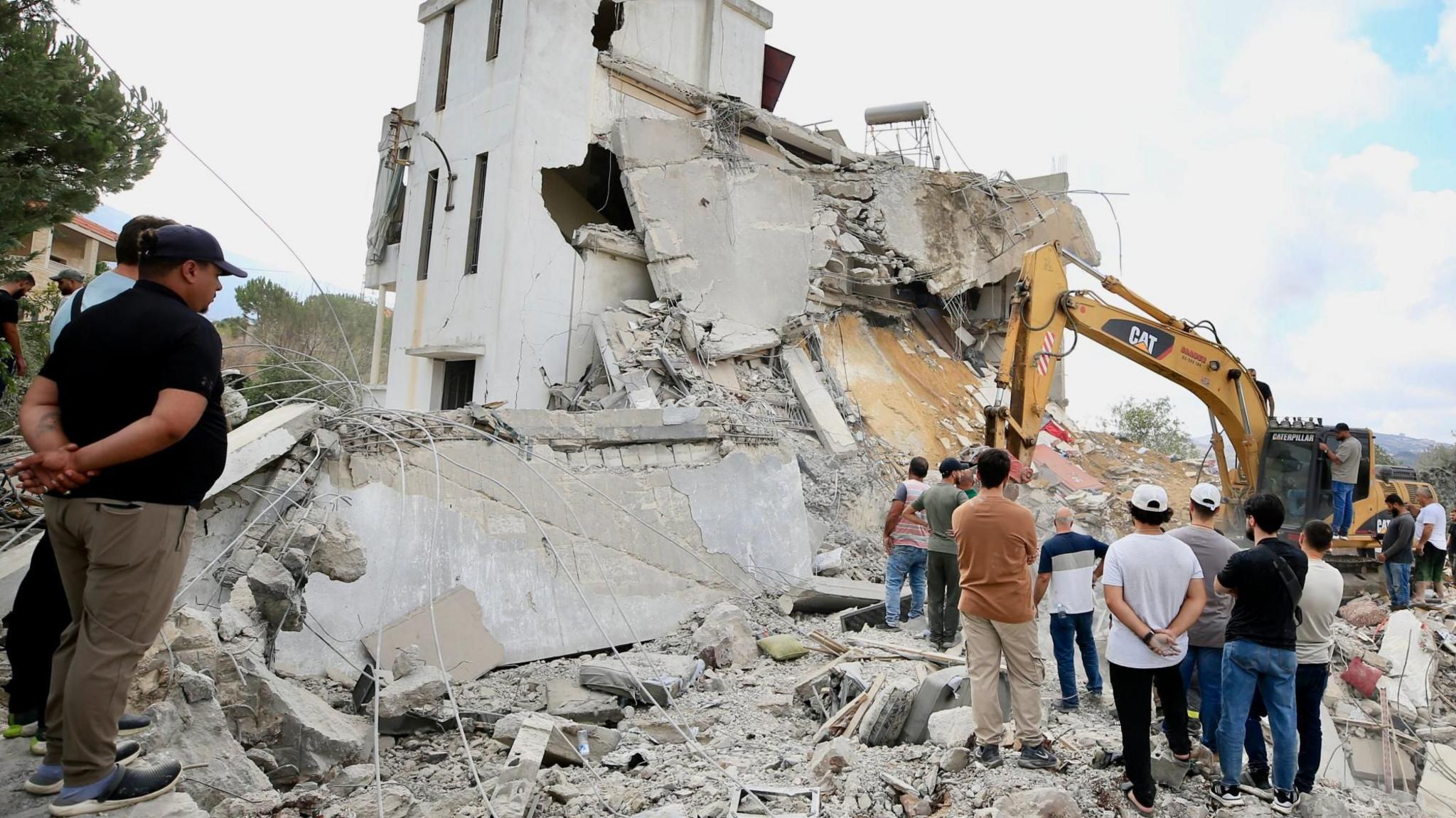 Men look at an excavator working at the site of an Israeli strike in Arab Salim, southern Lebanon