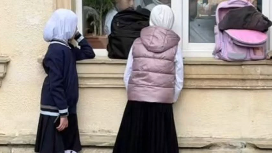 Two hijab-wearing schoolgirls at school window