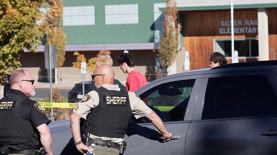 Two men in bullet‑proof vests stand near the school