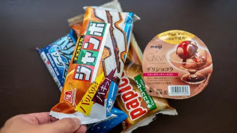 A stack of packaged Japanese ice‑cream, a hand holding one pack on top of three others